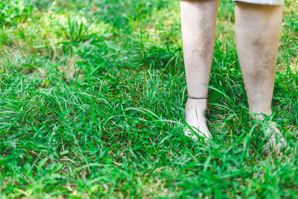 Молодая женщина, гуляющая босиком по траве парка весной. Девушка с браслетом на лодыжке отдыхает на свежем зеленом лугу. Концепция изображения для ухода за ногами
 - Фото, изображение
