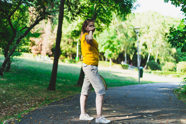 Młoda kobieta kichająca podczas spaceru po parku. Przypadkowo ubrana millenium dziewczyna o sezonowej alergii na świeżym powietrzu. Kobieta z grypą i objawami przeziębienia w okresie letnim - Zdjęcie, obraz