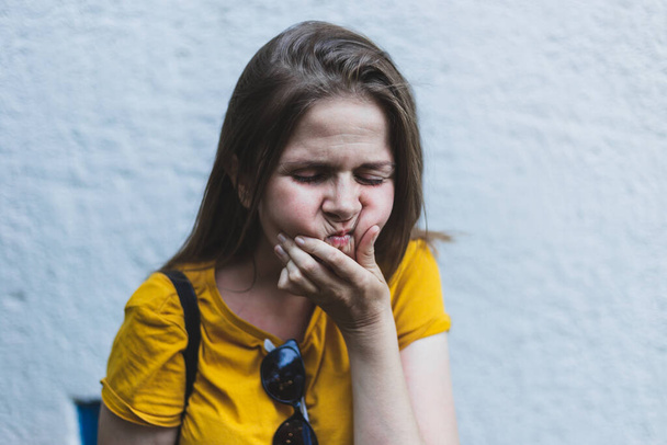 Young woman suffering from dental pain outdoors with copy space. Pretty girl with brown hair massaging her jaw while experiencing a toothache in the city. Portrait of sad female with inflamed mouth - Fotoğraf, Görsel