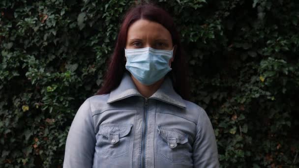 Portret van een vrouw met een medisch masker op haar gezicht in de natuur tijdens een Coronavirus pandemie. - Video