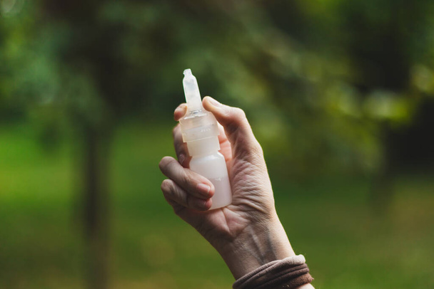 Mladá žena držící nosní sprej v přírodě. Ženská ruka s bílým příjemcem se používá k léčbě různých typů alergií a nemocí způsobených viry. Koncepční obraz pro zdravotnictví - Fotografie, Obrázek