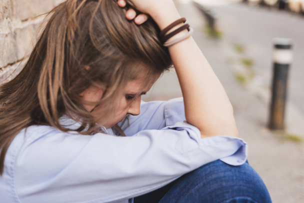 Smutna i przygnębiona młoda kobieta trzymająca głowę w jednej ręce na zewnątrz. Widok z boku pięknej zdenerwowanej kobiety myślącej siedząc na ławce w parku - Zdjęcie, obraz