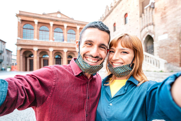 Happy boyfriend and girlfriend in love taking selfie with face masks at old town tour - Wanderlust life style travel concept with tourist couple on city sightseeing vacation - Bright warm filter - Photo, Image