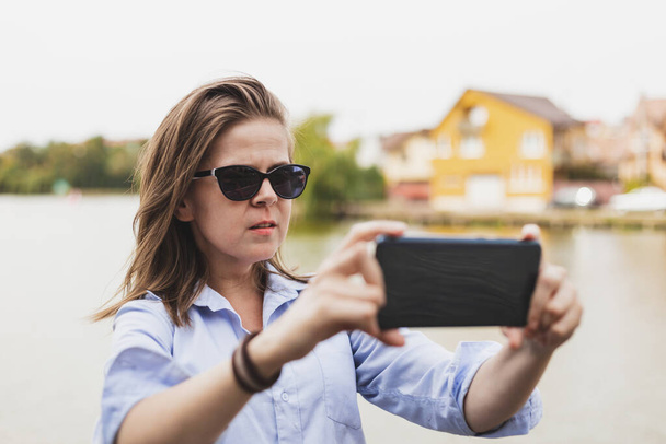 Young blogger recording a video for her next social media event. Teen holding mobile camera horizontally while recording her talking outside - Photo, Image