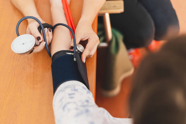 Sestra měřící krevní tlak od mladé ženy se stetoskopem v nemocnici. Žena zdravotní asistentka kontrola vitálních funkcí a zdraví pacienta v soukromé klinice - Fotografie, Obrázek