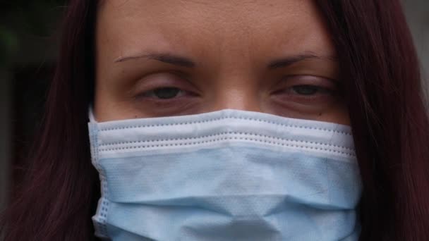 青い目の女性と医療用マスクの顔の上に. - 映像、動画