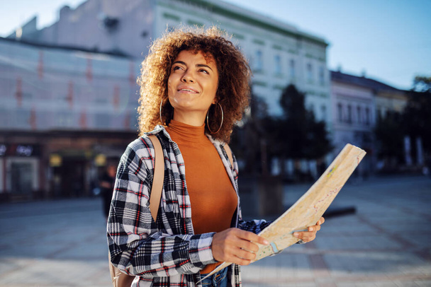 Молода приваблива жінка-туристка, що стоїть на площі, тримає карту і озирається навколо
. - Фото, зображення