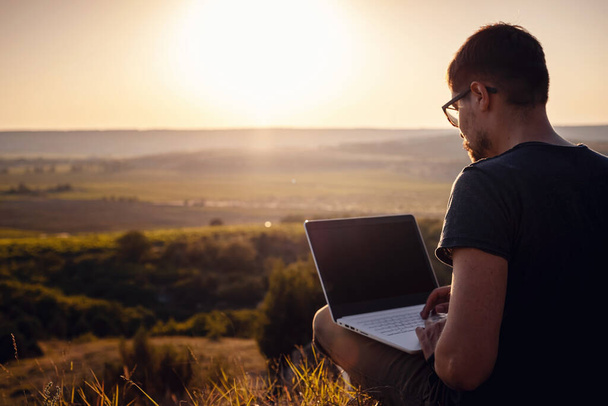 man with laptop sitting on the edge of a mountain with stunning views of the valley. Cellular network broaband coverage concept. 5G. - Foto, afbeelding
