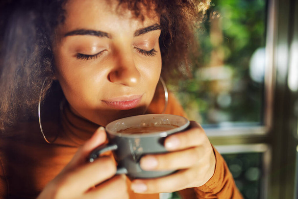 Крупный план смешанной расы женщина держит чашку кофе и нюхает его
. - Фото, изображение