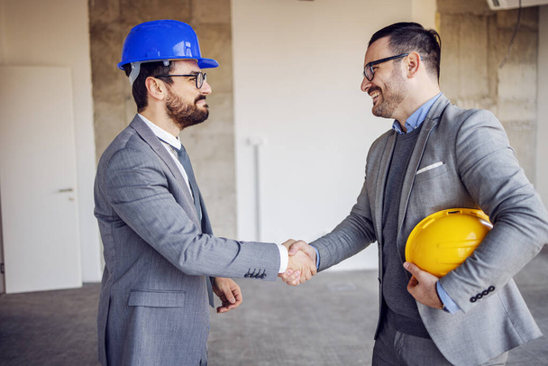 Real estate agent making a deal with businessman and shaking hands with him. Building in construction process interior. - Foto, Imagen