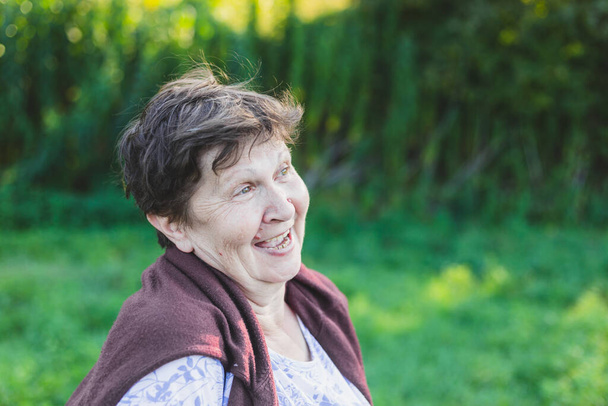 Portrait of beautiful senior woman laughing in nature. Happy smiling old lady daydreaming on a summer day outside. Elderly person enjoying life feeling carefree and relaxed - Фото, зображення