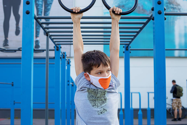 10 yaşında bir çocuk spor sahasında maske takıyor. Koronavirüsün sonuçları. Kendini ve çocuklarını koru. Spor yüzükleri. Fotoğraf. - Fotoğraf, Görsel