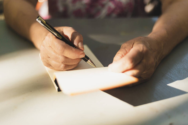Mujer tomando notas. Primer plano de las manos femeninas sosteniendo un bolígrafo y un cuaderno. Periodista escribiendo en entrevista
 - Foto, Imagen