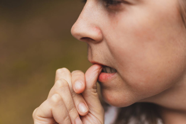 Zbliżenie kobiety trzymającej palec między zębami. Dziewczyna wykazuje oznaki niepokoju, trzymając kciuk między ustami - Zdjęcie, obraz