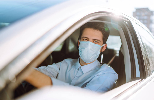 Man driving a car wearing on a medical mask during an epidemic, a driver- taxi in a mask. Covid-2019. - Zdjęcie, obraz