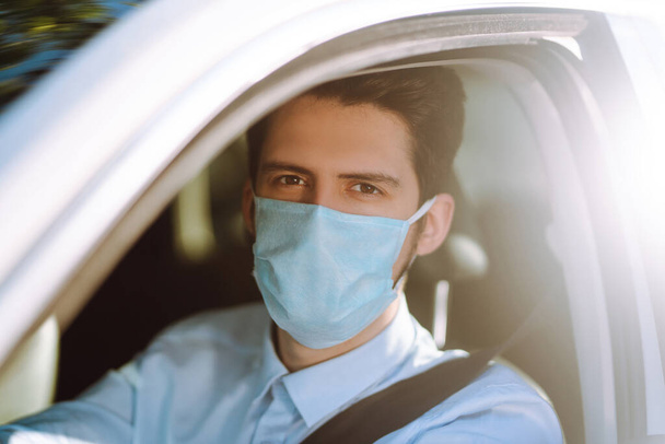 Man driving a car wearing on a medical mask during an epidemic, a driver- taxi in a mask. Covid-2019. - Photo, image