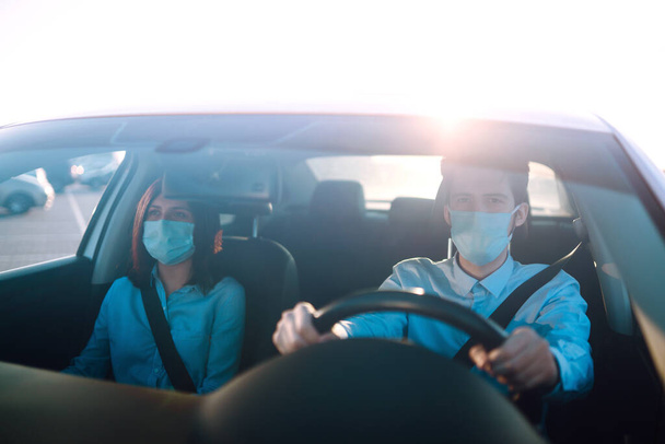Young man and woman  driving in a car during coronavirus quarantine in medical masks. Safe taxi, protection from the virus. Covid-2019. - Photo, Image