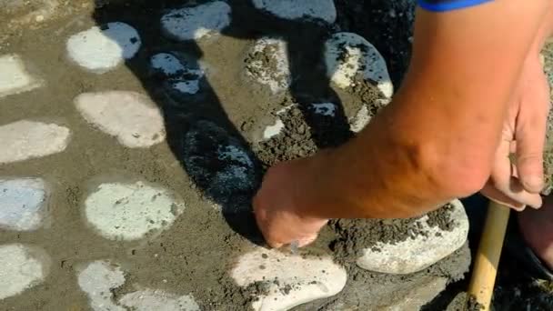 メイソンは道に石を積み込む。セメントからジョイントを洗浄します。色のついた石畳のモザイクに手仕事。日だ。晴れ。ジョージア. - 映像、動画