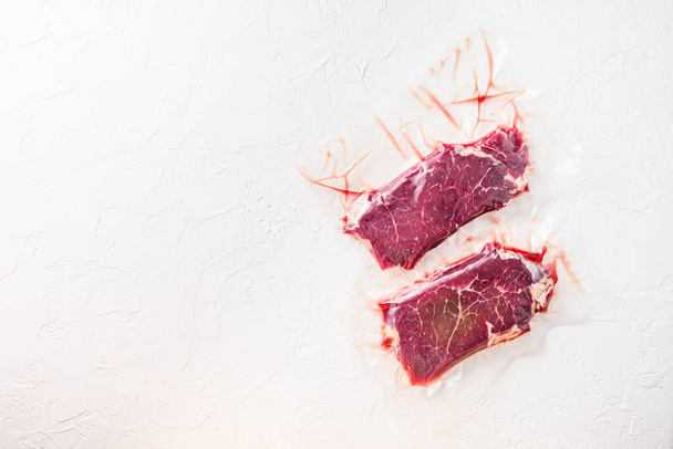 Sada vakuově balené bio hovězí maso rump steak na bílém betonu texturované pozadí, horní pohled prostor pro text - Fotografie, Obrázek