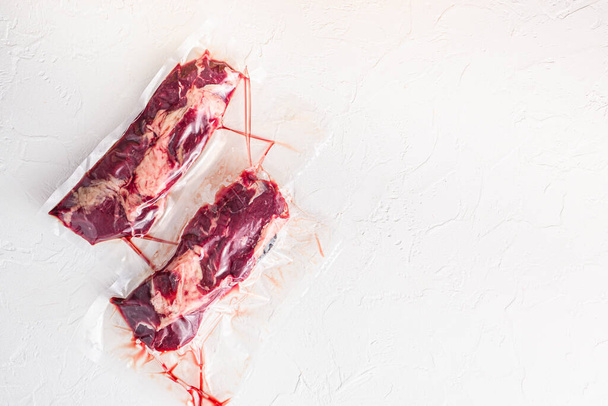 Пара ролл говяжий стейк, вакуумная упаковка органического мяса для су-виде приготовления пищи на белом бетонном текстурированном фоне, вид сверху для текста
 - Фото, изображение