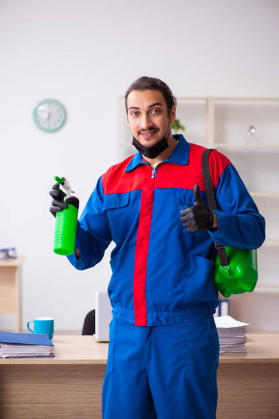 Contratista masculino joven desinfectando oficina - Foto, Imagen