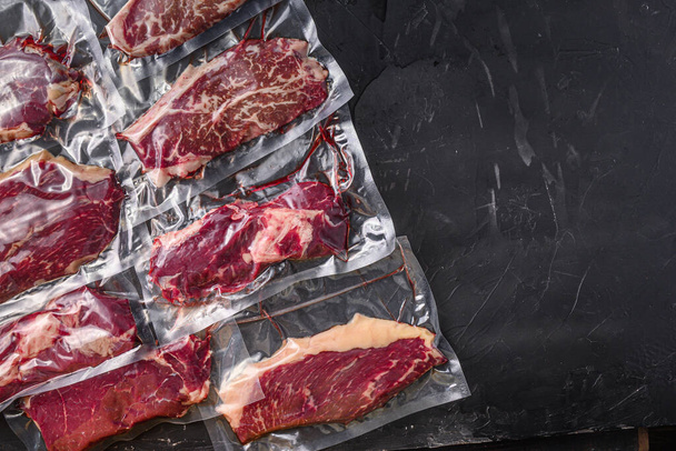 Süpürge paketlenmiş organik sığır eti alternatif kesimler: üst bıçak, popo, picanha, chuck roll biftekleri, siyah desenli arka plan, metin için üst görünüm alanı - Fotoğraf, Görsel