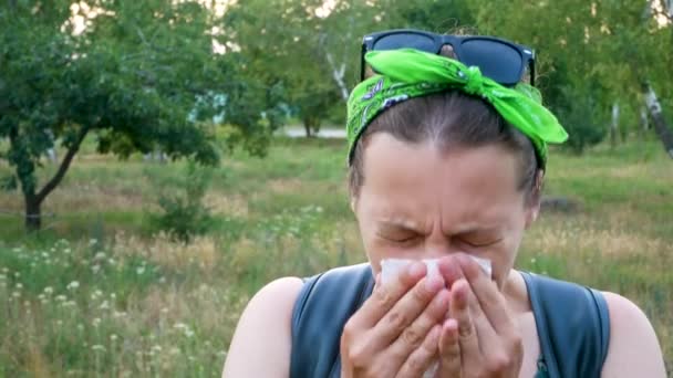 Donna con sintomo di allergia al polline aria odorosa con naso in piedi su sfondo natura estiva. Giovane ragazza malata starnutisce, soffia il naso nel fazzoletto, usando spray nasale contro la rinite allergica - Filmati, video