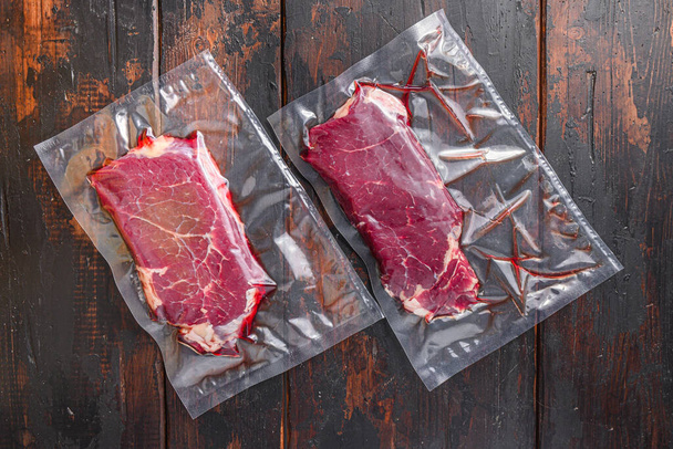 Vákuum csomagolt Rump Steak szerves marhahús sötét régi fa asztal, felülnézet - Fotó, kép