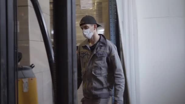 Serious man in face mask getting into warehouse loader. Portrait of confident male employee working at factory on Covid-19 pandemic quarantine. Profession, employment, lifestyle, logistics. - Video