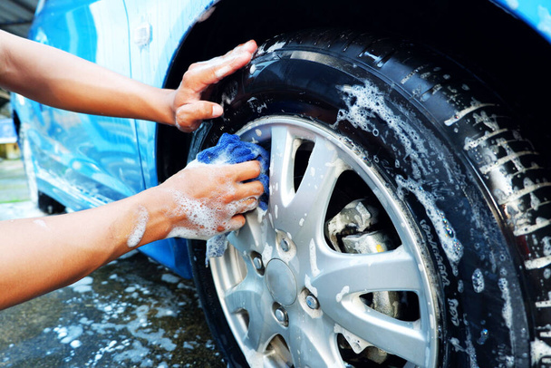 マイクロファイバークロスで車の車輪を掃除しながら車を洗う - 写真・画像
