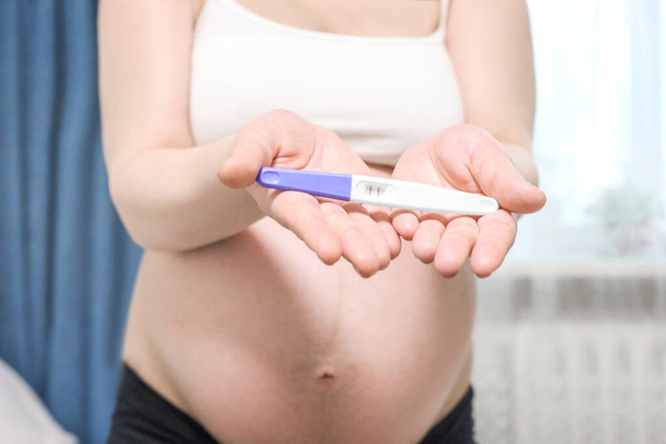 Happy pregnant woman holding pregnancy test with beautiful belly that pregnant girl has fetus inside. Young Mother waiting newborn baby prenatal, pregnancy, motherhood, expecting concept - Photo, Image