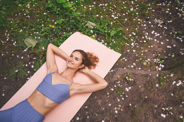 Kaunis sovi nainen urheiluvaatteet tekee harjoituksia vaaleanpunainen jooga matto. Lihaksikas hoikka houkutteleva nainen tasainen vatsa kesäpuistossa ulkona. Kehonhoito, terveellinen, kunto, urheilullinen elämänkonsepti - Valokuva, kuva