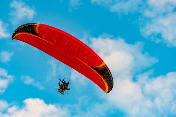 Red dome of a motor paraglider flying on a background of blue cloudy summer sky. Tandem on a paraglider high in the sky. - Photo, image