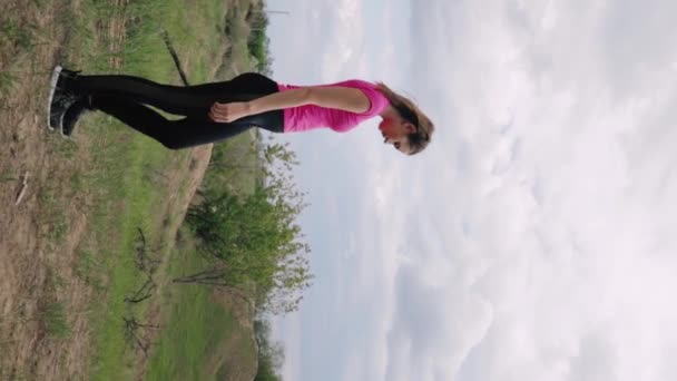 Young woman in sportswear stretching and warming up on hill before physical exercises. Fitness, healthy way of life, wellbeing concept. - Footage, Video