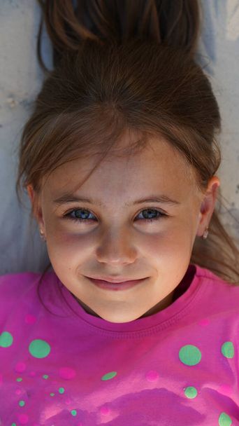 Retrato de una niña muy sonriente vestida de rosa tumbada en la arena
 - Foto, Imagen