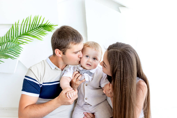 young mom and dad kissing a child, parents with their son in a photo Studio, family day, happy family - Photo, Image