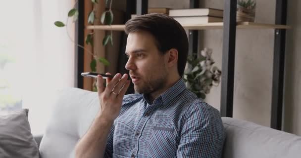 Man sit on couch holding smartphone makes call using speakerphone - Πλάνα, βίντεο