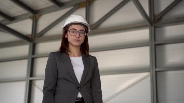 Eine junge Frau mit Schutzhelm zeigt auf einer Baustelle einen Daumen. Die Chefin im Anzug blickt in die Kamera. - Filmmaterial, Video