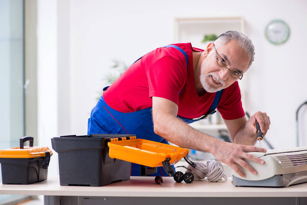 Старый мужчина-подрядчик ремонтирует кондиционер в помещении
 - Фото, изображение