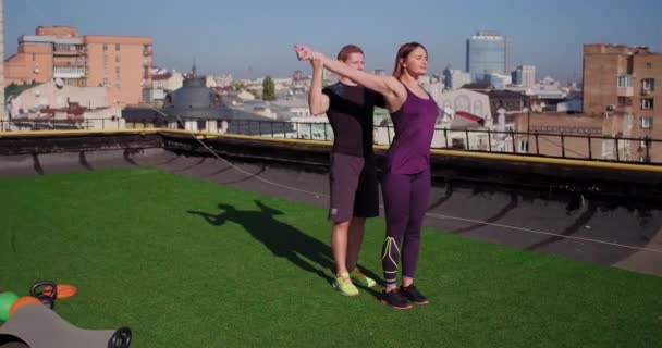 Sportive couple of man and woman in sportswear, doing stretching exercise on roof of building, urban background. Prores 422 - Кадры, видео