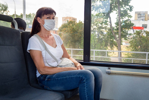 Adult woman in a protective mask rides alone in an empty on public transport in the city. Social distance. Bus passengers are protected from the coronavirus. New normal. lifestyle during the pandemic - Valokuva, kuva