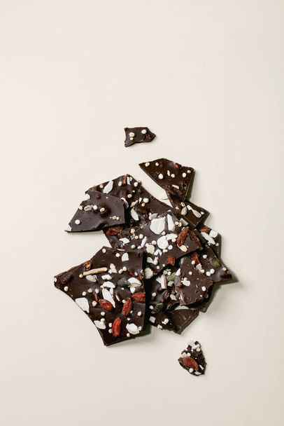 Handmade chopped dark chocolate with different superfood additives seeds and goji berries over beige background. Flat lay, copy space - Photo, Image