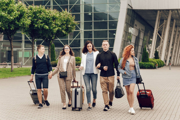 Gelukkige positieve jongeren met bagage buiten in de buurt van de luchthaven. Vrienden die terugkomen van een reis. Reizen en vakantie concept - Foto, afbeelding