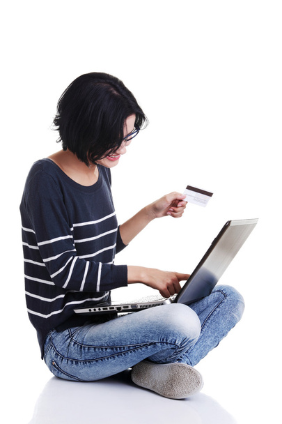 Mujer con un portátil y una tarjeta de crédito, sentada en el suelo, iso
 - Foto, imagen