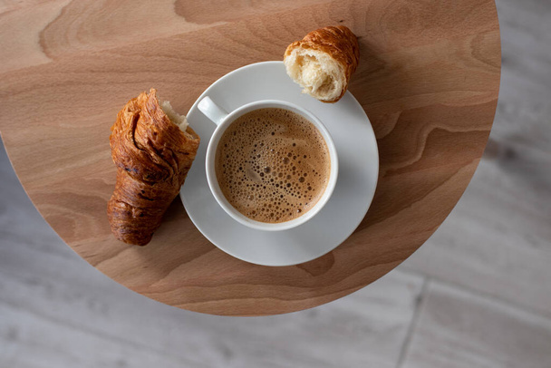 Modern french breakfast Top view. White cup of hot coffee with fresh baked croissant on the round wooden table - Фото, изображение