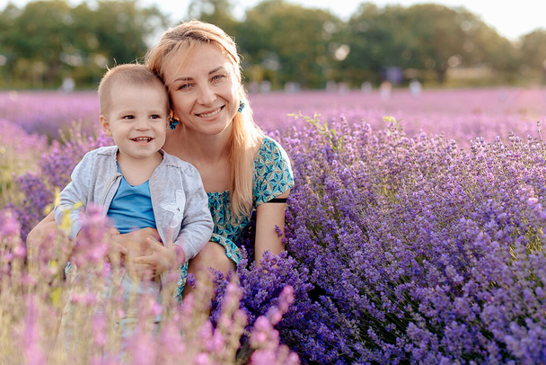 Happy young mother and her little son posing in purple field of lavender flowers - Foto, Bild