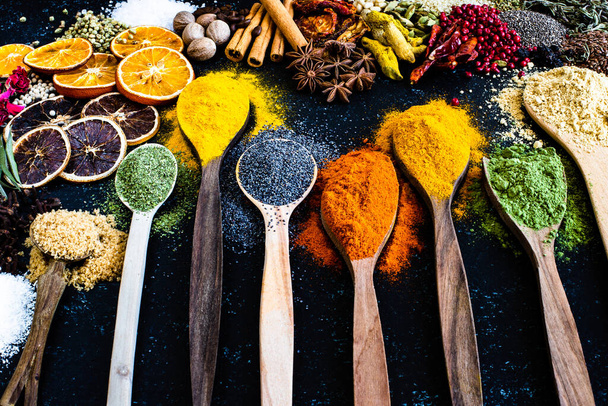 Many colorful spices, herbs and dried fruits on the wooden rustic table. Spices in the spoons and bowls with top view.  - Photo, Image