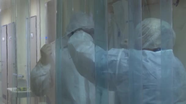 Het medisch personeel verzorgt de behandeling en desinfectie van kleding in de "vuile zone" onder ultraviolet licht, wegwerp antivirale pakken. - Video