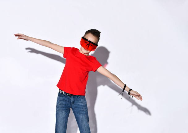 Teenage boy in oversized sunglasses with protective visor, red t-shirt and jeans. Spread hands, smiling, posing isolated on white - Valokuva, kuva