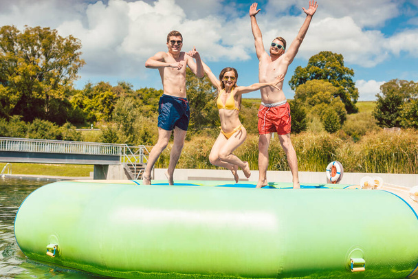 Friends having fun jumping off a big tuby thing in public pool - Photo, Image